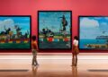 Three paintings hang on a wall in a museum.