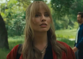 Margot Robbie looking curiously forward with Colin Farrell walking in the background behind her on the right. .
