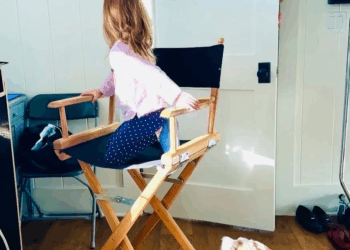 Princess Lilibet sitting in a directors chair turning to look at Daniel Martin peeking from a doorway