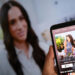 A person holds a smartphone displaying Netflix's new Meghan Markle show, "With Love, Meghan", in front of a TV screen showing footage of the show.