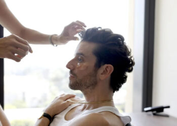 A man with patches under his eyes being groomed by a person off camera.