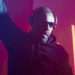 Idris Elba wearing headphones and sunglasses, he is a DJ at an event with bright red lights behind him