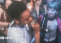 The artist is singing into the microphone passionately. The audience infront of her are dancing and enjoying the music.