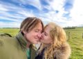 Nicole Kidman kisses Keith Urban on the cheek under a blue sky with white clouds.