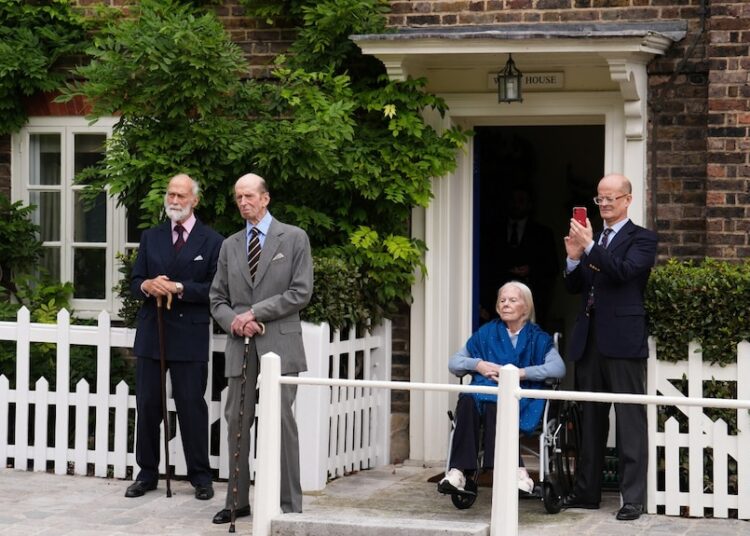 Three men and a woman who is sitting in a wheelchair outside a home, looking on.