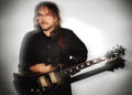 Jeff Tweedy in glasses and a flannel shirt holding a guitar