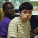 Two teenagers in a cafeteria turn their heads in surprise while holding lunch items