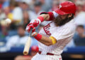 Philadelphia Phillies outfielder Brandon Marsh swings bat while wearing white uniform and red helmet