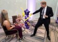 A man in a suit plays with a balloon near a young girl who is sitting down. Another woman who's also sitting is looking on.