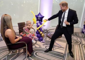 A man in a suit plays with a balloon near a young girl who is sitting down. Another woman who's also sitting is looking on.