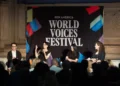 Four panelists sit on stage in front of a PEN America World Voices Festival banner, engaging with an audience, with one person signing in American Sign Language.