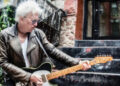 Ricky Byrd wears a weathered biker jacket and throws a pose as he plays a Telecaster on the stoop of a NYC apartment.