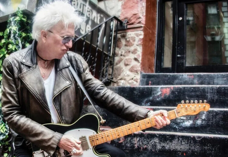 Ricky Byrd wears a weathered biker jacket and throws a pose as he plays a Telecaster on the stoop of a NYC apartment.