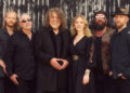 Robert Plant and Saving Grace standing against a corrugated fence.