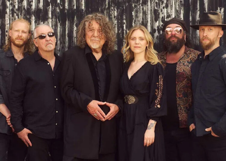 Robert Plant and Saving Grace standing against a corrugated fence.