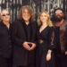 Robert Plant and Saving Grace standing against a corrugated fence.