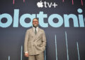 Seth Rogen in a suit stands in front of a backdrop with the Apple TV+ logo and the word