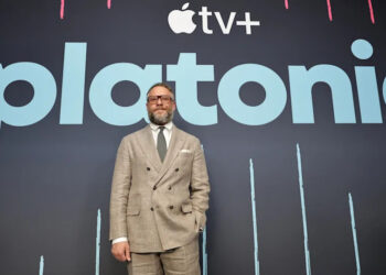 Seth Rogen in a suit stands in front of a backdrop with the Apple TV+ logo and the word