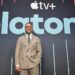 Seth Rogen in a suit stands in front of a backdrop with the Apple TV+ logo and the word
