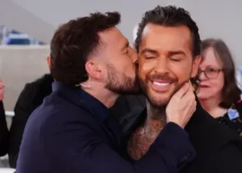 PA Media A man with short black hair kisses another man with long slicked black hair on his cheek.