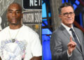 Charlamagne tha God in a white t-shirt with an eagle design, and Stephen Colbert in a gray suit and glasses, gesturing with his hand.