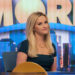 Reese Witherspoon as Bradley Jackson smiling at something off camera and sitting in front of The Morning Show sign in The Morning Show season 4.