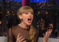 A person is animatedly talking on a talk show, wearing a sheer-sleeved outfit with a side braid