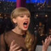 A person is animatedly talking on a talk show, wearing a sheer-sleeved outfit with a side braid