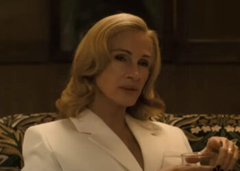 Julia Roberts sitting down in a white blazer and a drink in hand in After The Hunt.