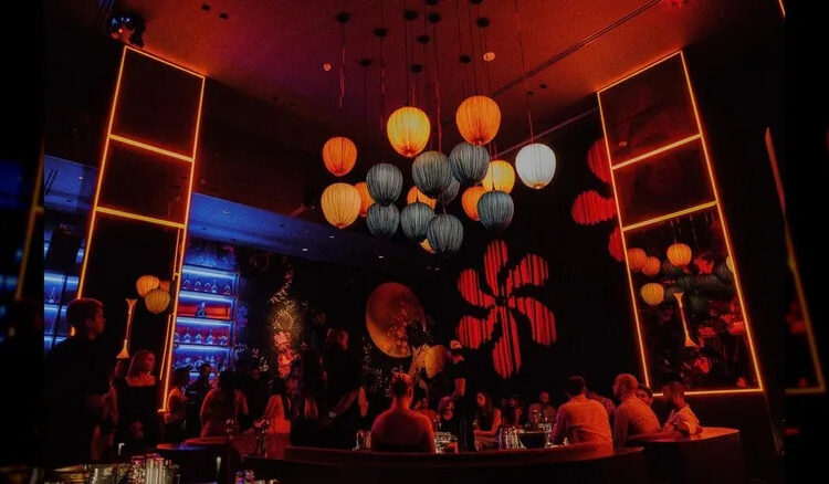 Lounge space at Gekkō, with red lighting, a blue backlit bar, and paper lanterns over center VIP seating