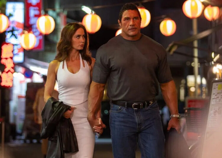 From left to right: Emily Blunt walking and holding hands with Dwayne Johnson in The Smashing Machine. .
