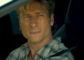Glen Powell looking wistful staring out a car window wearing earrings in Chad Powers trailer.  .