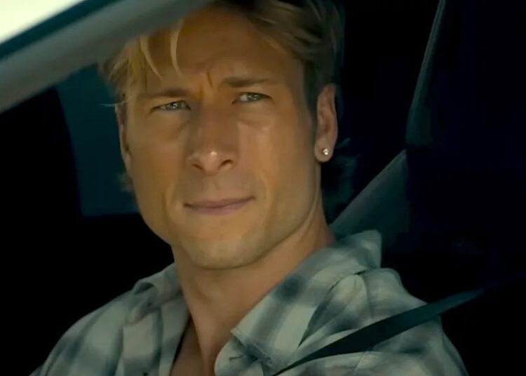 Glen Powell looking wistful staring out a car window wearing earrings in Chad Powers trailer.  .