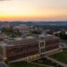 An aerial drone shot shows the Evansdale area of campus with the Agricultural Sciences building in the forefront and a golden skyline in the background.