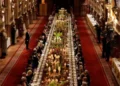 PA A long dining table with dignitaries seated down either side is seen in a banquet hall, with staff and press against the walls.