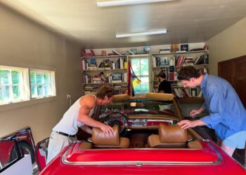 two individuals working on a classic red convertible car in a garage