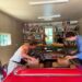 two individuals working on a classic red convertible car in a garage