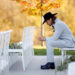 Jesse McBee in a grey suit and black hat, sitting among empty charis at his wedding and looking down at the ground with his hands folded