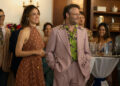 a woman in a polka dot dress stands next to a man in a pink suit at a large party