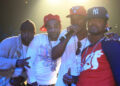 Cam'ron, Jim Jones, Juelz Santana, and Freekey Zekey on stage, wearing casual and urban-style clothes, with baseball caps and jewelry, posing for a photo