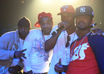 Cam'ron, Jim Jones, Juelz Santana, and Freekey Zekey on stage, wearing casual and urban-style clothes, with baseball caps and jewelry, posing for a photo