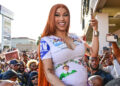 Cardi B, smiling and holding a phone, in a crowd wearing a colorful dress.
