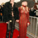 Pamela Anderson and Tommy Lee holding hands on the red carpet at the American Music Awards in 1997, Anderson in a sheer red patterned dress with a large black hat