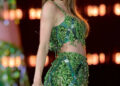 Taylor Swift performs on stage wearing a shimmering, fringed outfit with intricate patterns and holds a blue microphone