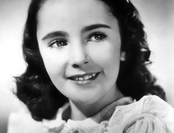 A young girl with wavy hair and a smile, wearing a ruffled blouse, poses for a portrait