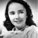 A young girl with wavy hair and a smile, wearing a ruffled blouse, poses for a portrait