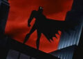 Batman stands silhouetted on a rooftop against a dramatic sky, cape flowing