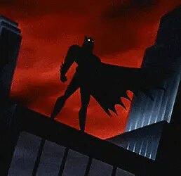 Batman stands silhouetted on a rooftop against a dramatic sky, cape flowing