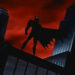 Batman stands silhouetted on a rooftop against a dramatic sky, cape flowing