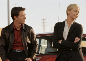 Croker and Stella talk, leaning on the hood of a car, in The Italian Job